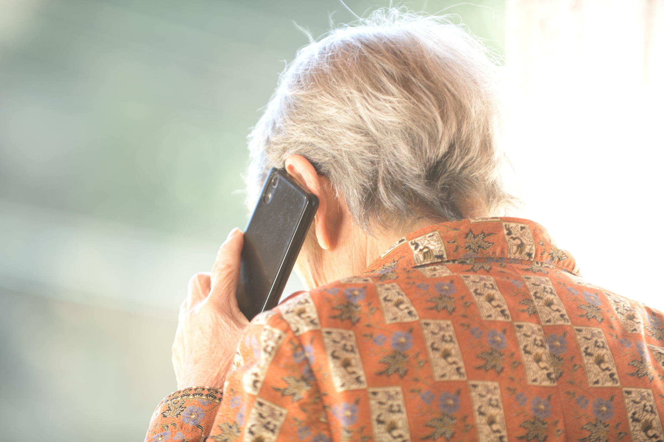 view of an elderly individual on the phone from behind