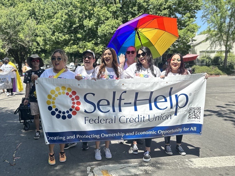 happy people holding a Self-Help Federal Credit Union banner