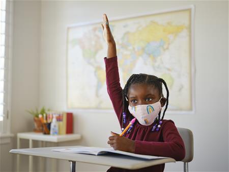 cdfi-iStock-1258026134 Masked child raising hand in a classroom