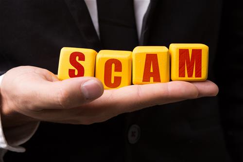 iStock-687793954 Hand holding block letters that spell "SCAM"